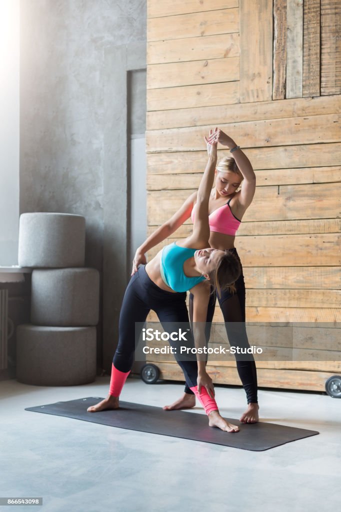 Young woman with yoga instructor in fitness class, triangle pose Yoga class instructor helps beginner to make asana exercises. Teacher assists to make triangle pose, trikonasana. Healthy lifestyle in fitness club. Stretching with coach 20-29 Years Stock Photo