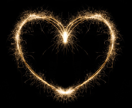 New year party burning sparkler heart shape on black background. Glowing holiday sparkling hand fireworks, love symbol shining fire flame. Christmas light.