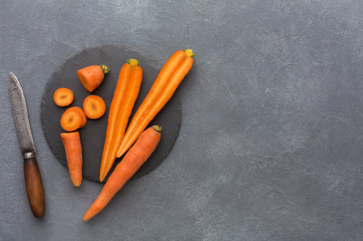 Cut carrots on rustic slate stone plate. Cooking healthy food on gray background, copy space, top view.