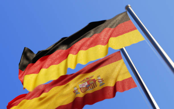 High quality 3d render of German and Spanish flags waving with wind on a blue sky. Low angle view with copy space and selective focus. Great use for German and Spanish politics related concepts. Horizontal composition.