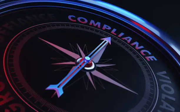 Arrow of a compass is pointing compliance text on the compass. Arrow, compliance text and the frame of compass are metallic blue in color. Red light illuminating compass is creating a sense of tension. Black backgound. Horizontal composition with copy space. Compliance concept.