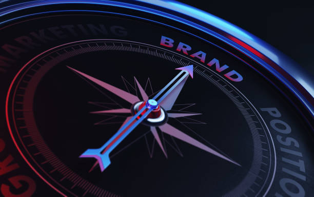 Brand Concept: Arrow of A Compass Pointing Brand Text Arrow of a compass is pointing brand text on the compass. Arrow, brand text and the frame of compass are metallic blue in color. Red light illuminating compass is creating a sense of tension. Black backgound. Horizontal composition with copy space. Brand concept. position stock pictures, royalty-free photos & images