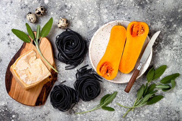 istock Raw ingredients for making black pasta with butternut squash, parmesan cheese and sage. Concrete background, top view, flat lay. Halloween black and orange party dinner concept 866604710
