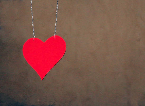 istock Metal red heard hung as a sign with two chains againd dark beige wall 866604928