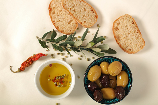 Green and black olives in porcelain bowl with olive oil  with fresh bread, young olive branch , thyme and pepper on white background.