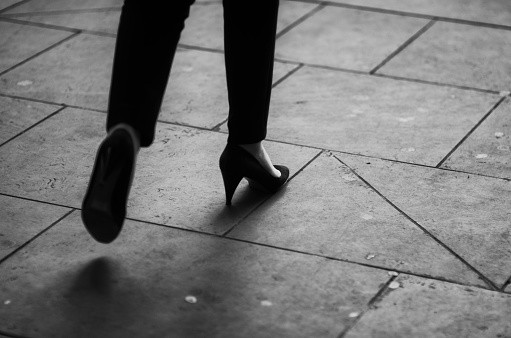 Close-up of the high heels of a businesswoman walking on the gritty city sidewalk in black and white