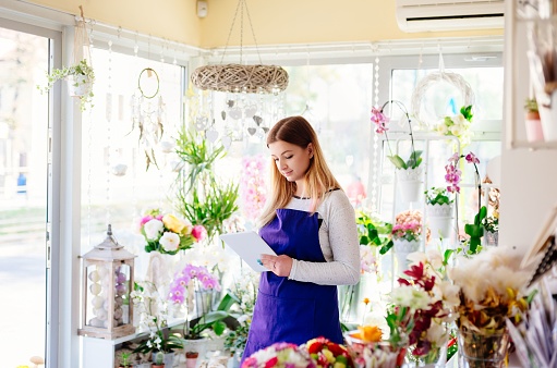 Woman owner of florist shop taking orders online by tabletWoman owner of florist shop taking orders online by tablet