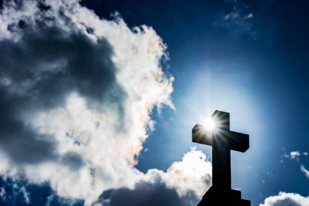 Religious cross against cloudy sky with sunlight