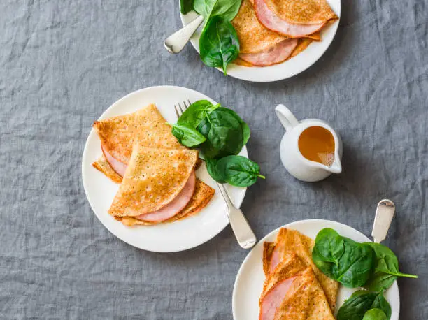 Photo of Crepes with ham and spinach. Delicious, nourish breakfast on a grey background, top view