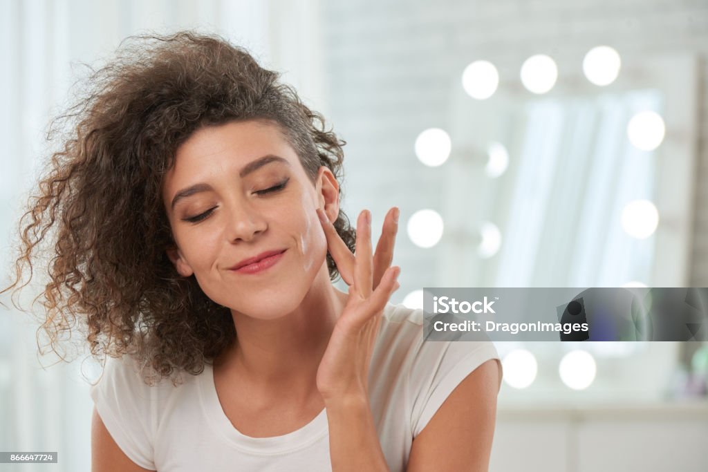 Enjoying smooth skin Smiling woman applying serum on her face Moisturizer Stock Photo