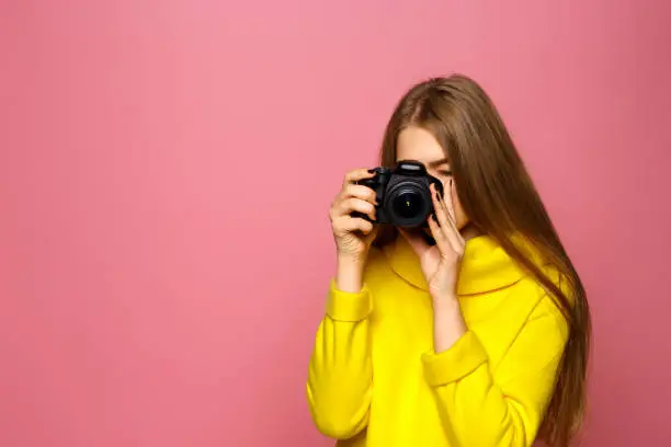 Girl photographer! Beautiful young girl takes a picture. In a yellow sweater on a pink background. Copy space