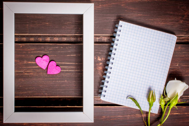 istock two hearts in photo frame and blank notebook with copyspace and white rose flower on wooden background. greeting card . 866656534