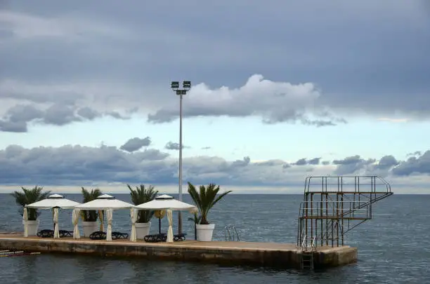 abandoned pier with white umbrellas in a beach-resort in Croatia, ocean in the background, cloud-formations in the sky