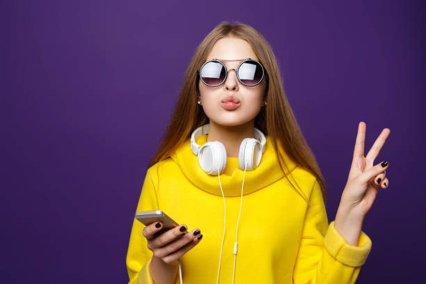 イヤホンと携帯電話、黄色いセーターの肖像若い女の子のティーンエイ ジャーは、紫色の背景に分離します。 - modern girl ストックフォトと画像