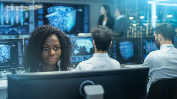 female computer engineer works on a neural network/ artificial intelligence project with her multi-ethnic team of specialist. office has multiple screens showing 3d visualization. - teamwork medical research science women imagens e fotografias de stock