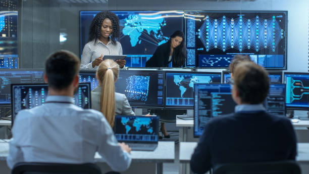 istock Chief Project Engineer Consults Tablet Computer and Holds Briefing for a Team of Scientists that are Building Machine Learning System. Displays Show Working Model of Neural Network. 866661512