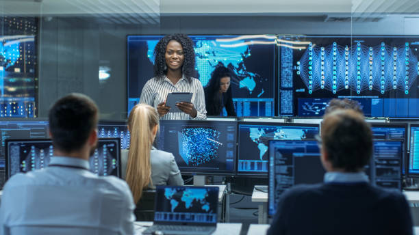 istock Chief Project Engineer Consults Tablet Computer and Holds Briefing for a Team of Scientists that are Building Machine Learning System. Displays Show Working Model of Neural Network. 866661596
