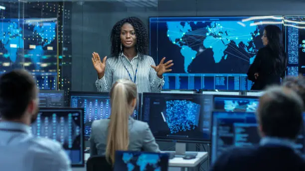 Photo of Chief Project Engineer Holds Briefing for a Team of Scientists that are Building Machine Learning System. Displays Show Working Model of Neural Network.