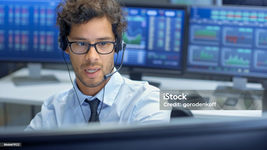 Courtier en faisant des ventes avec un casque d’écoute avec son équipe multiethnique de Stock Traders au bureau de cabinet de la bourse est occupé vente et achat d’obligations et actions. Affiche spectacle graphiques pertinents et les numéros. - Photo de Centre d'appel libre de droits