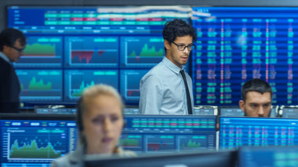 istock Stock Trader Inspects Others Work and Chat with Other. Busy Office with Multi-Ethnic Team of Brokers, Dealers. Displays Show Numbers and Infographics. 866662126