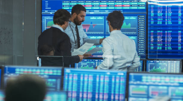 istock Three Experienced Stock Traders Talking Business, Consulting Documents and Argue About Data. They Work for a Big Stock Exchange Firm. Office is Full of Displays Showing Infographics and Numbers. 866662264