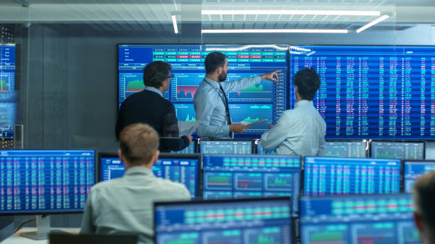 istock Three Experienced Stock Traders Talking Business, Consulting Documents and Argue About Data. They Work for a Big Stock Exchange Firm. Office is Full of Displays Showing Infographics and Numbers. 866662310