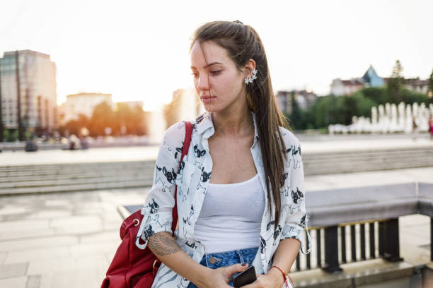 Young woman feeling depressed Sad brunette woman sitting on the footbridge, holding her mobile phone and looking away pensively dream believe tattoo stock pictures, royalty-free photos & images