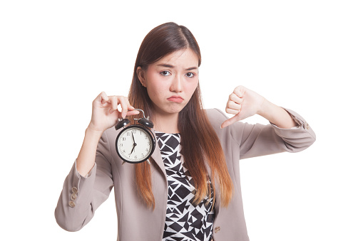 Young Asian woman thumbs down with a clock isolated on white background