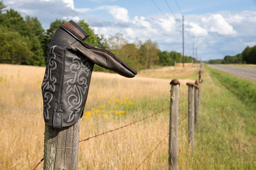 Cowboy boot on a barbed wire fence post.  Concepts could include rural culture, traditions, western life, humor, others.