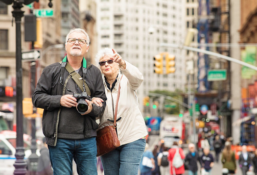 Senior couple discovering New-York City in Autumn. On this photograph, the male is holding a camera and looking up at a building his female partner is pointing to enthusiastically.