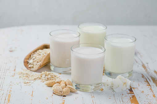 Non-dairy milk alternatives in glasses on white wood background