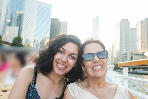 Senior Hispanic Woman and Millennial Granddaughter on Chicago Boat Tour This is a horizontal, color photograph of a two beautiful Puerto Rican women from different generations are enjoying a boat tour in Chicago, Illinois, a major USA city in the Midwest. The senior grandmother and Millennial granddaughter pose together, smiling as they look at the camera. Buildings along the Chicago River fill the background. puerto rican ethnicity stock pictures, royalty-free photos & images