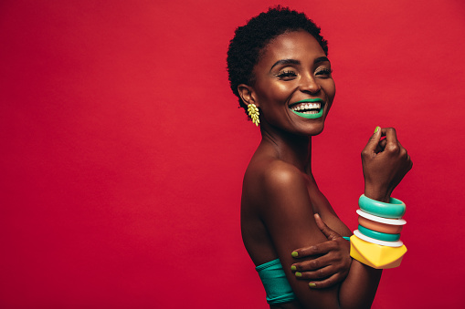 Beautiful young african woman with vivid makeup against red background. Smiling female model wearing artistic makeup looking at camera.