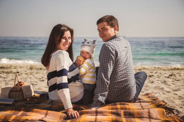 jeune famille aimante heureux avec petit enfant, profiter de temps à la plage, assis et des caresses près océan, notion de famille de style de vie heureux - beach on child the photos et images de collection