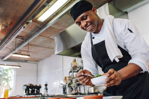 Gourmet chef cooking in a commercial kitchen Gourmet chef in uniform cooking in a commercial kitchen. Happy male cook wearing apron standing by kitchen counter preparing food. preparing food stock pictures, royalty-free photos & images