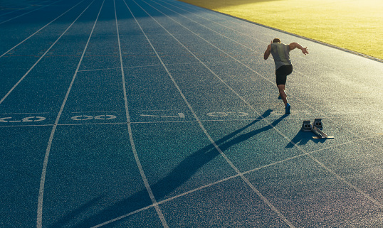 Athlete running on an all-weather running track alone. Runner sprinting on a blue rubberized running track starting off using a starting block.