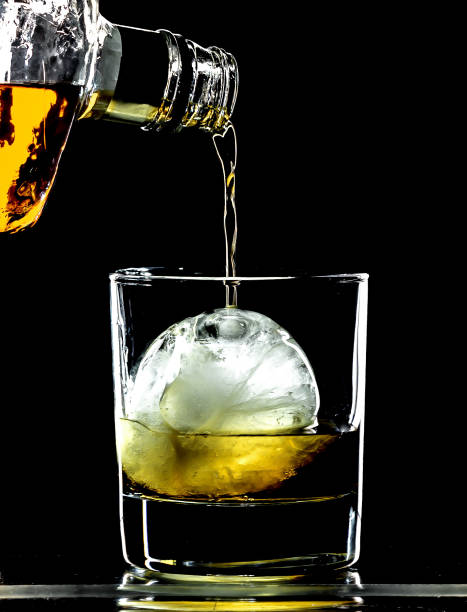 istock Round spherical ice cube ball in a cocktail glass with unique rim lighting against a black background, with an alcoholic beverage being poured into it. 866725830