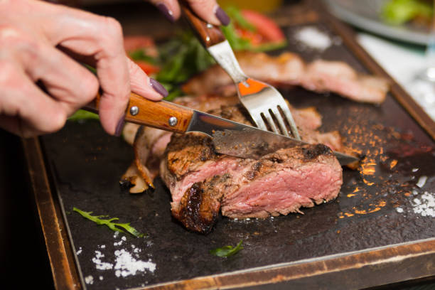 main de femme tenant le couteau et coupe fourche grillée bifteck - horizontal steak dinner food photos et images de collection
