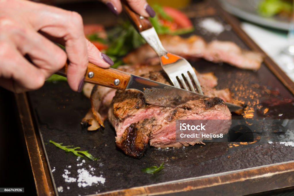 Woman hand holding knife and fork cutting grilled beef steak Woman hand holding knife and fork cutting grilled beef steak on stoned plate. Selective focus Meat Stock Photo