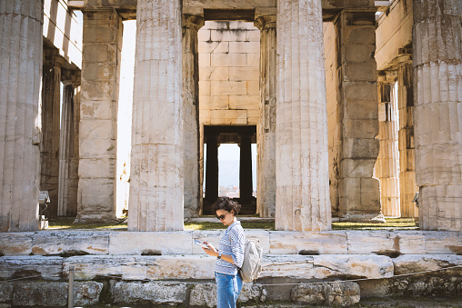 Young woman visiting the Ancient Agora of Athens. Holding a brochure standing by the columns of Temple of Hephaistos.