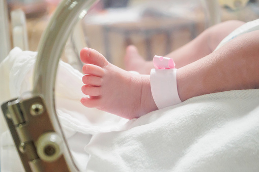 Bebé niña recién nacido dentro de la incubadora en el hospital con el nombre de la etiqueta de identificación pulsera photo