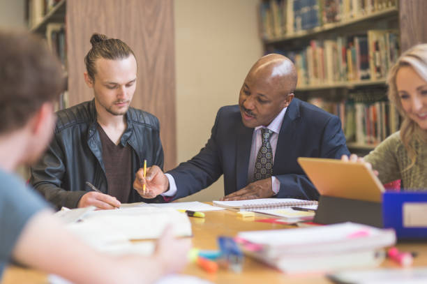 istock College students study together in the university library. An African American professor is helping them. 866793192