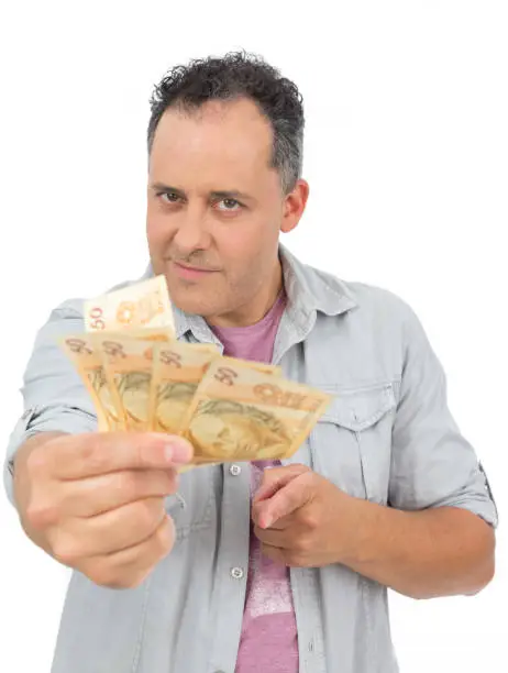 Photo of Man holds banknotes of money in his hand. Comnice of loan, payment, wealth, economy. Currency: Real Brasil. He is bald and wearing a gray shirt. Isolated on white background.