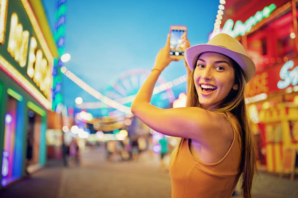 chica feliz está tomando fotos con su teléfono móvil en un parque de atracciones - niñas fotos fotografías e imágenes de stock