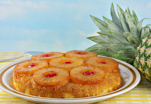 Pineapple upside down cake with a fresh whole pineapple to the side.  Blue sky background has copy space.