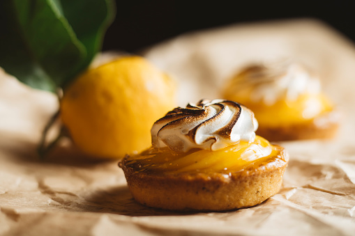 Lemon pie on the table with citrus fruits. Traditional french sweet pastry tart. Delicious, appetizing, homemade dessert with lemon cream. Copy space, closeup. Selective focus. Toned.
