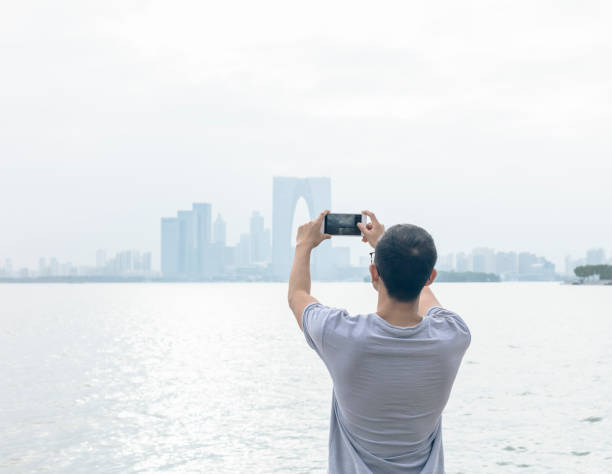 istock man standing on waterfront and taking shots with smartphone 866823148