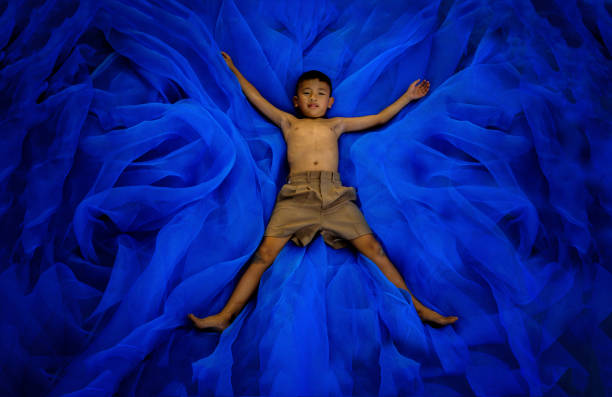 学生の少年パンツ学校制服睡眠や遊び場の青い blackground で床で遊んで、彼は飛ぶことができる、タイの田舎を信じる - conutryside ストックフォトと画像