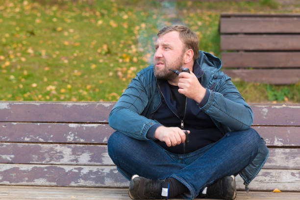 istock Young man smoking tobacco pipe in autumn park 866890552