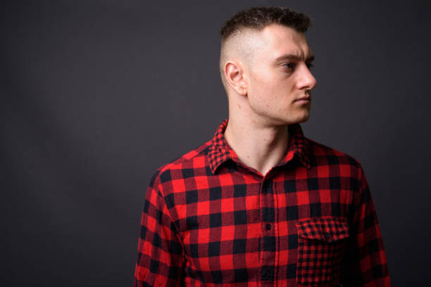 Young handsome man wearing red checked shirt against gray background Studio shot of young handsome man wearing red checked shirt against gray background half shaved hairstyle stock pictures, royalty-free photos & images